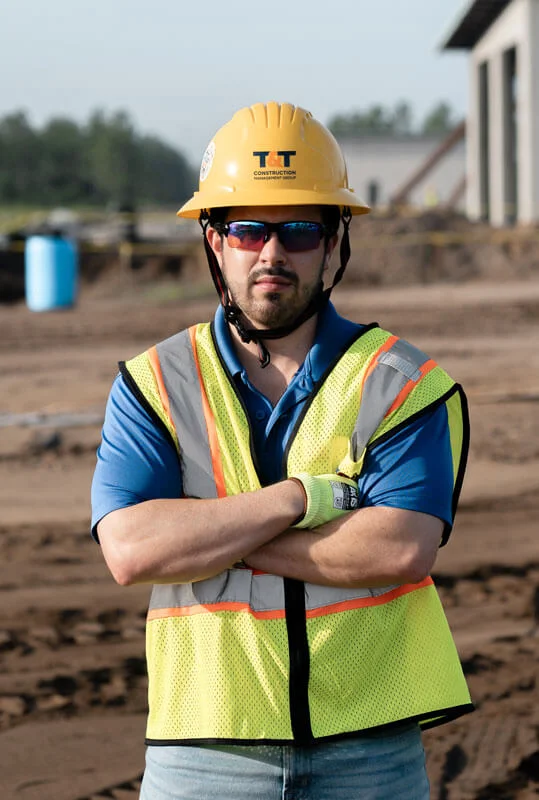man in the field crossing his arms, wearing a yellow construction hat